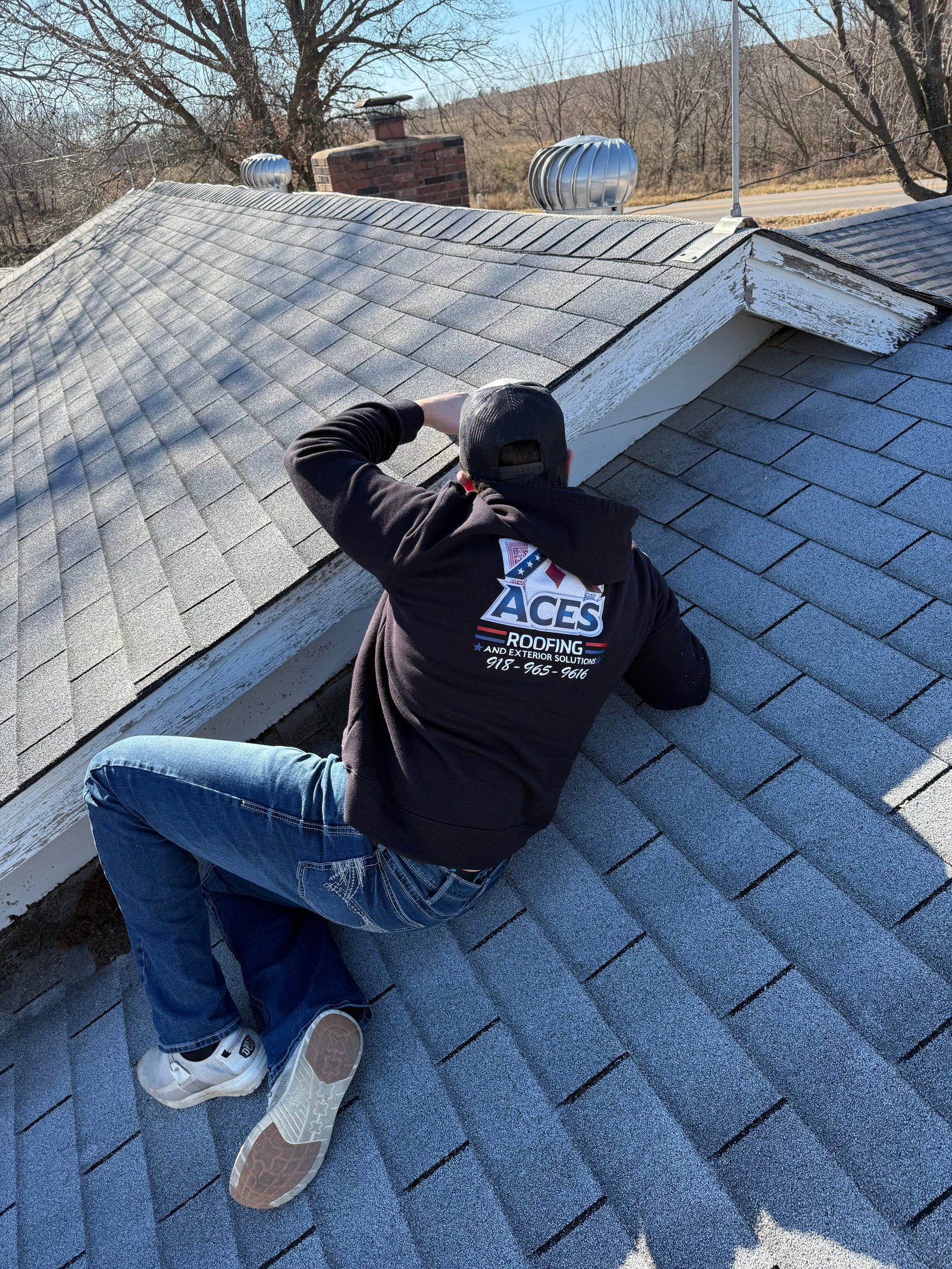 Storm damage roof inspection in Claremore Oklahoma. Licensed roofer from Aces Roofing and Exterior Solutions checking asphalt shingles along ridge line for hail or wind damage on residential roof.