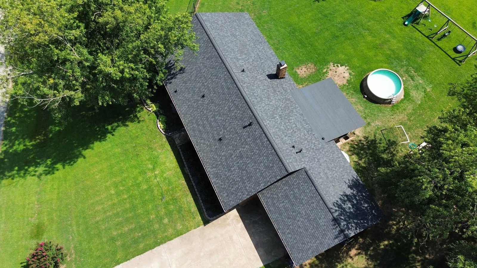 Aerial view of completed Owens Corning shingle roof in Inola, OK alongside the self-adhered flat roof section, with in-ground pool and playground in the backyard