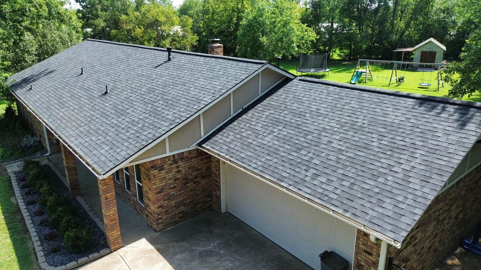 Angled aerial view of completed Class 3 Impact Resistant Owens Corning roof in Onyx Black on a brick home in Inola, OK, showing the garage, driveway, and gable roofline.