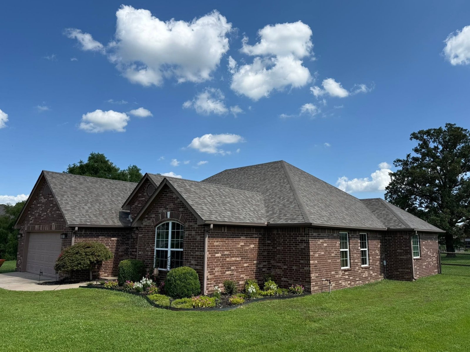 Side elevation of Claremore, OK brick home showing hip and gable roof lines after Owens Corning Duration roof installation by Aces Roofing and Exterior Solutions