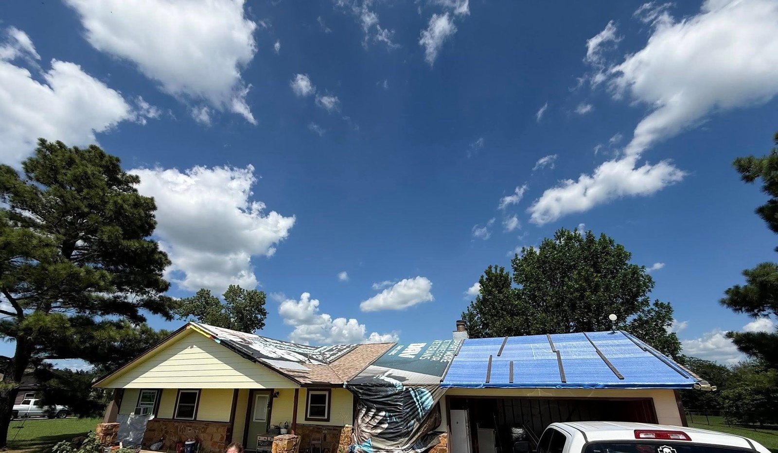 Wind damage roof repair in Claremore OK showing emergency tarp installed over tornado-damaged roof deck and storm-stripped shingles on residential home